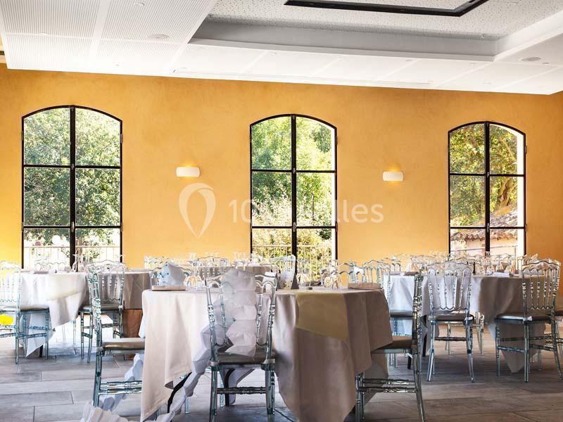 Salle lumineuse avec des tables dressées, des chaises transparentes et de grandes fenêtres donnant sur un extérieur…