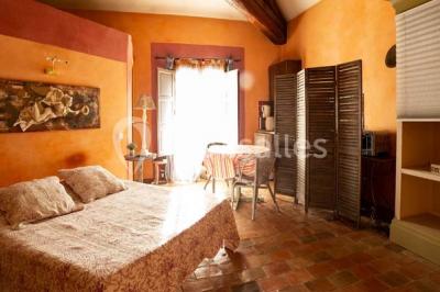 Chambre lumineuse avec murs orange, lit double, sol en terre cuite, table près d'une fenêtre et cloison en bois.