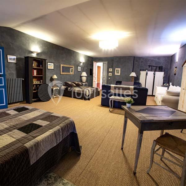 Grande chambre avec lits, canapé, bureau, étagères et éclairage doux, décorée dans des tons neutres et chaleureux.