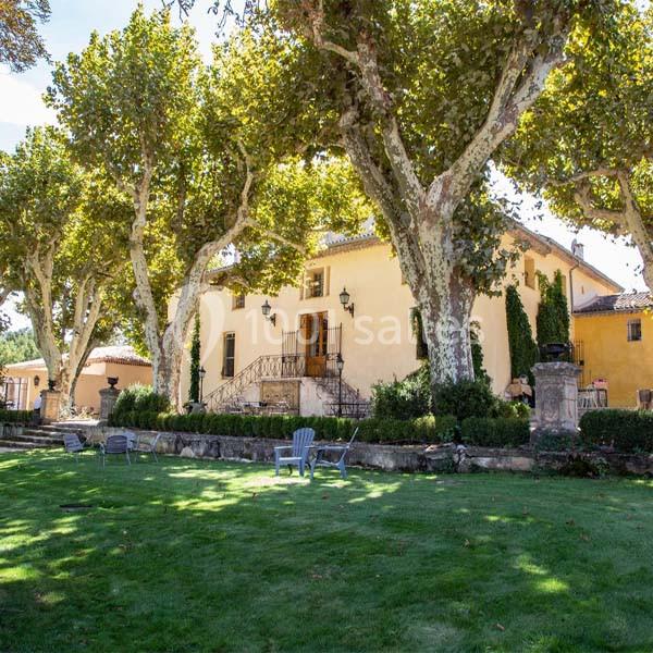 Grande maison en pierre entourée d'arbres et d'une pelouse bien entretenue, avec des chaises disposées sur le gazon.