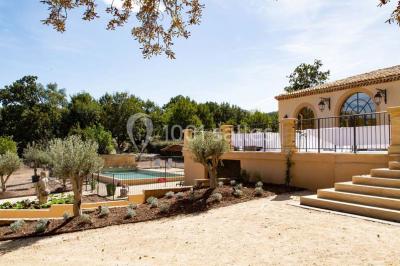 Façade d'une maison méditerranéenne avec terrasse, jardin aménagé et statues, entourée d'arbres sous un ciel dégagé.