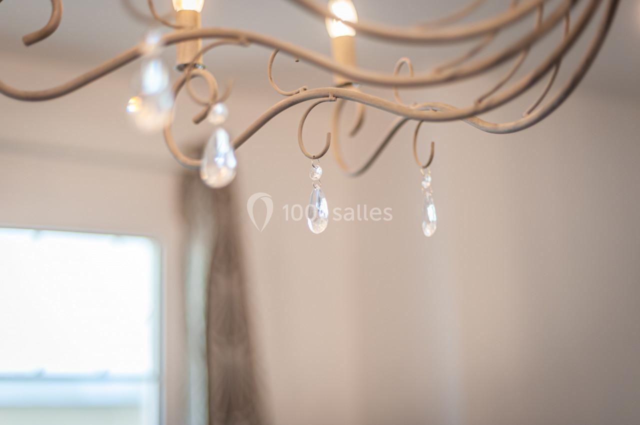 Lustre en métal avec pampilles en verre suspendues, éclairé dans une pièce lumineuse avec un fond flou.