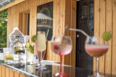 Maison entourée de verdure avec un chemin en gravier, des arbres et une terrasse visible en arrière-plan.