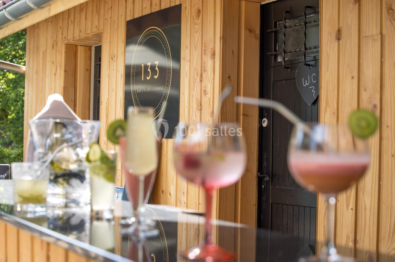 Verres de cocktails colorés posés sur un comptoir en extérieur devant un bâtiment en bois.