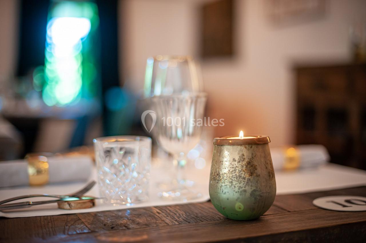 Bougie allumée sur une table en bois avec des verres et des couverts, dans un intérieur lumineux et flou en arrière-plan.