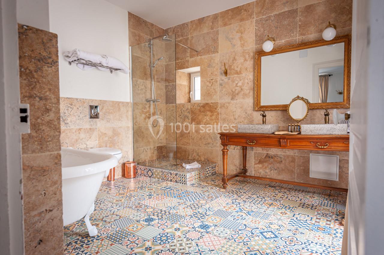 Salle de bain avec baignoire sur pieds, douche à l'italienne, carrelage coloré et meuble en bois avec miroir.