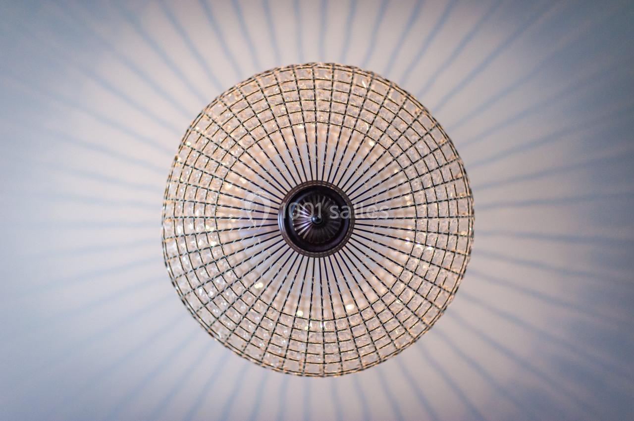 Vue en contre-plongée d'un lustre circulaire en verre avec des motifs rayonnants projetés sur le plafond.