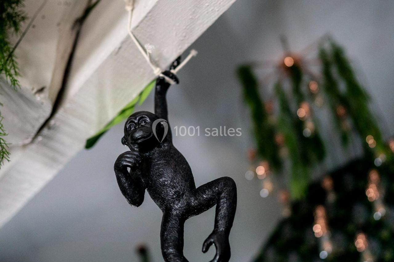 Singe décoratif noir suspendu à une poutre en bois dans une pièce ornée de plantes et de lumières.