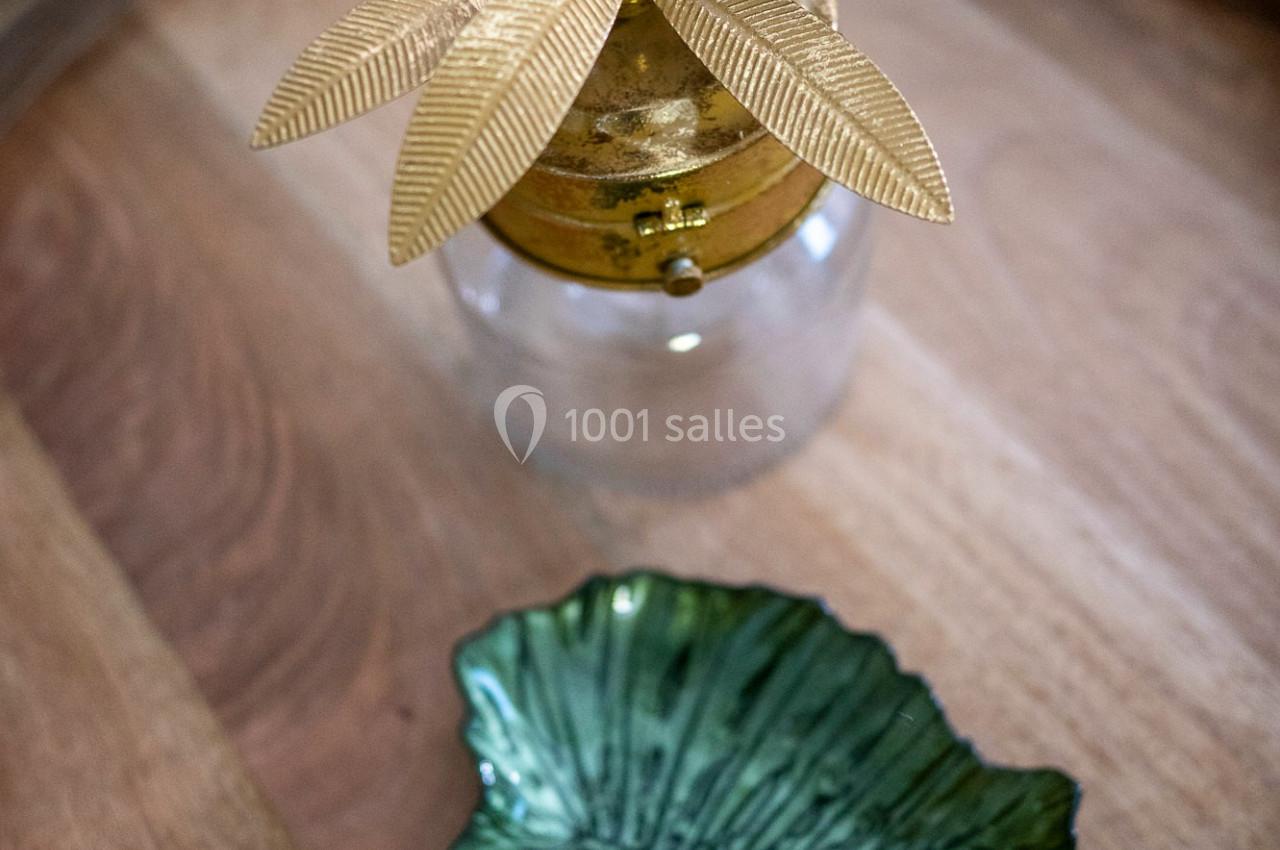 Objet décoratif doré en forme de feuilles et petite assiette verte en céramique sur un plateau en bois.