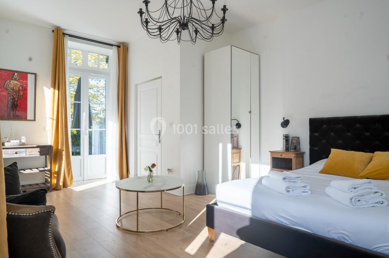 Chambre lumineuse avec lit double, table basse, armoire, bureau, grandes fenêtres et rideaux jaunes.