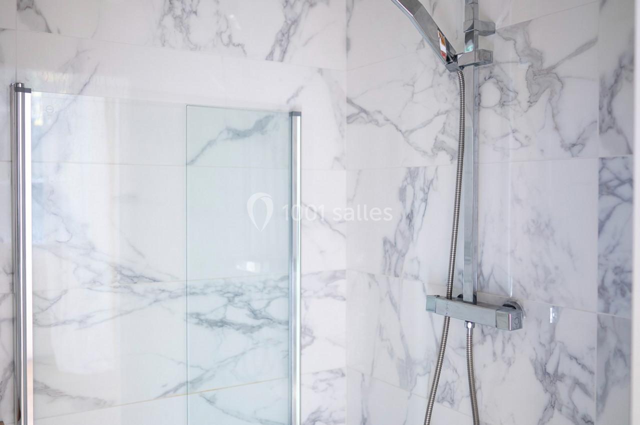 Douche moderne avec paroi en verre et carrelage effet marbre, équipée d'une colonne de douche chromée.