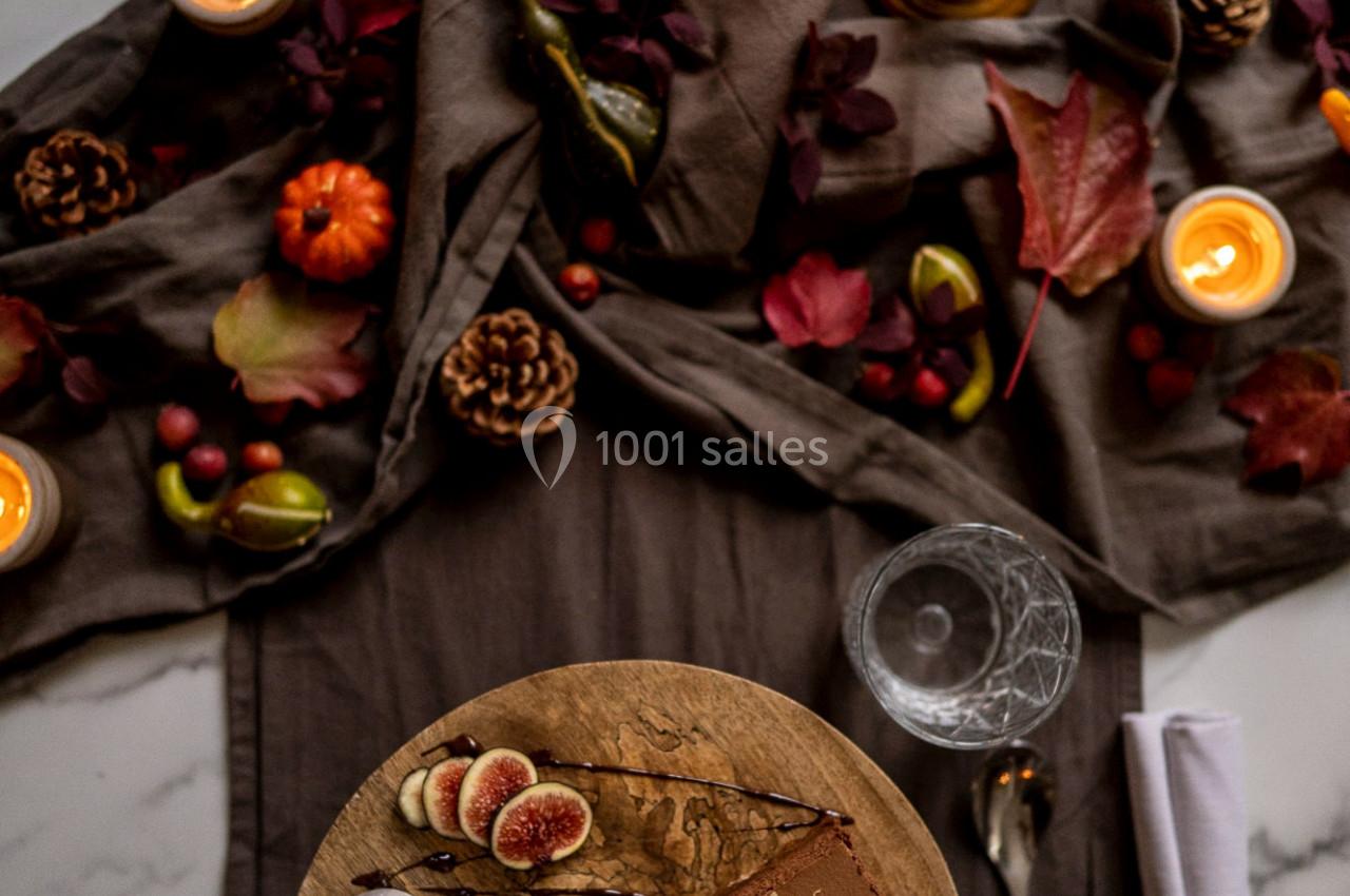Table décorée avec des bougies, feuilles d'automne, fruits, et dessert servi avec verre de vin et couverts.