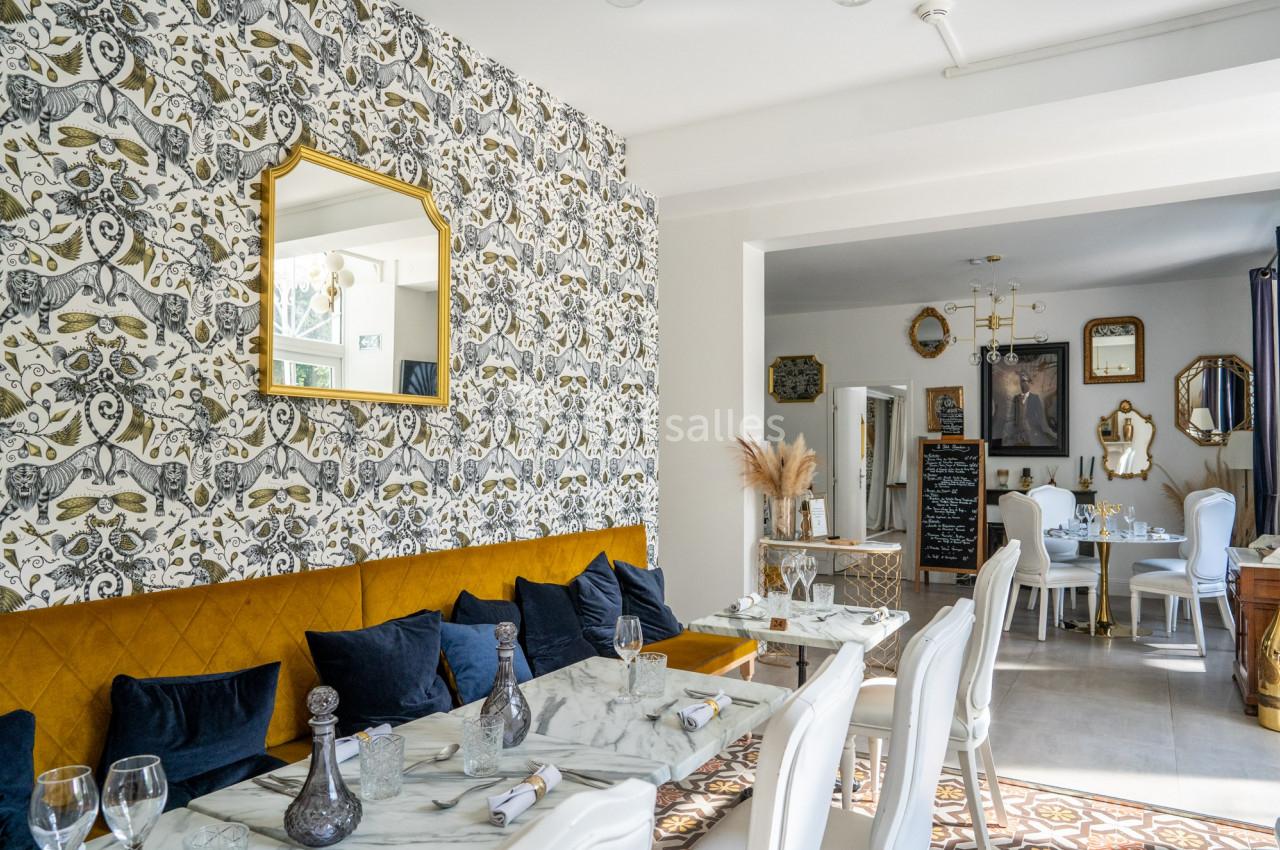 Salle de restaurant lumineuse avec tables en marbre, banquette jaune, chaises blanches et décoration murale élégante.