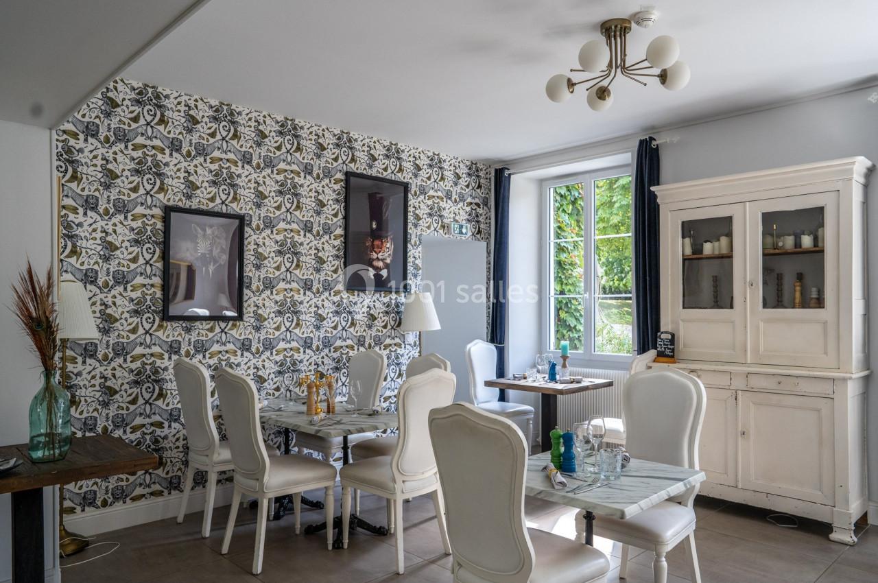 Salle à manger lumineuse avec des chaises blanches, des tables en marbre, un buffet ancien et un mur à motifs.