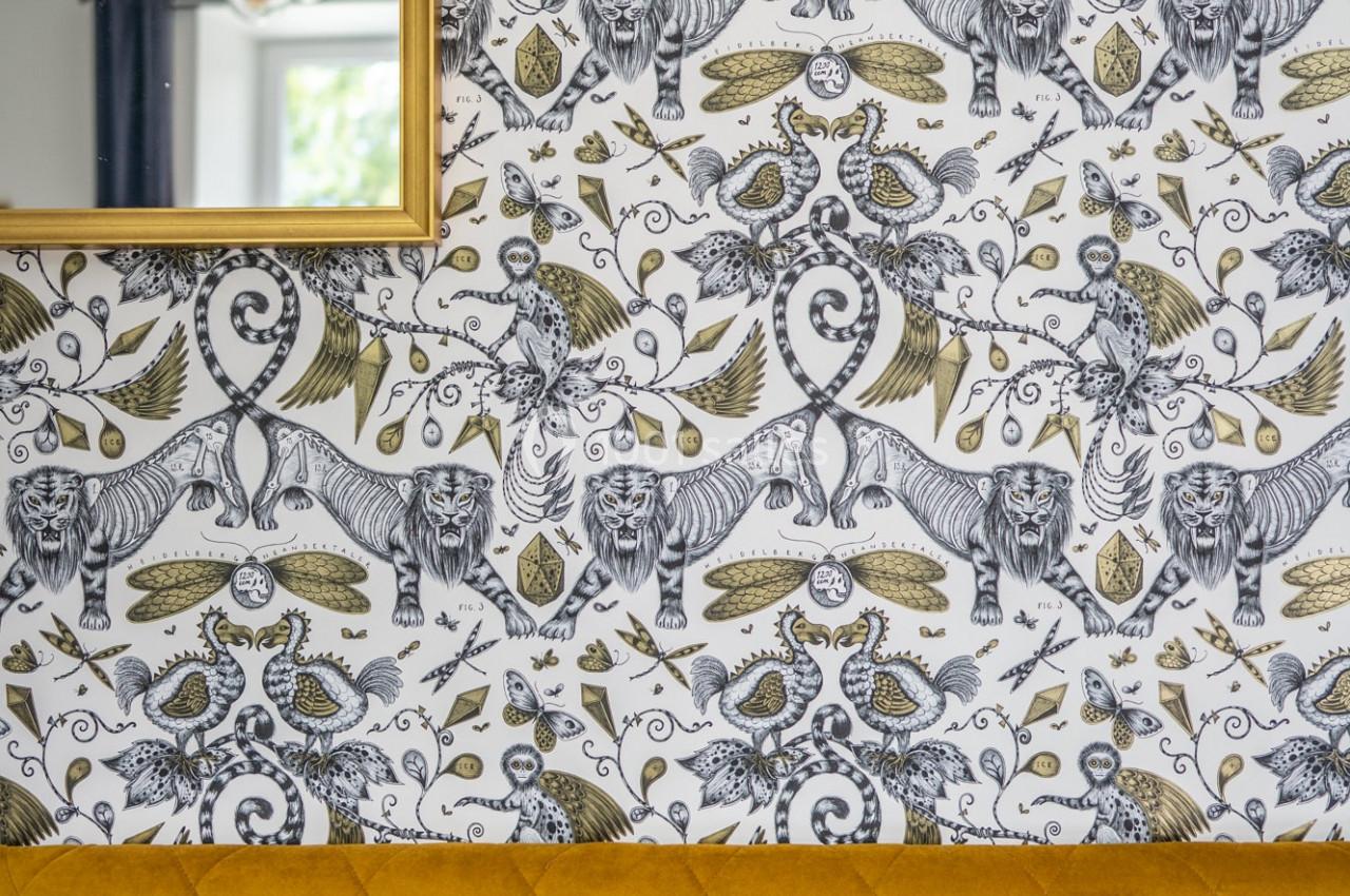 Papier peint à motifs animaliers et végétaux en noir, blanc et doré, avec un canapé jaune et des coussins bleus au premier…