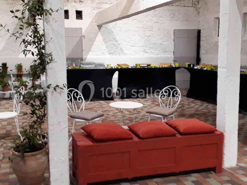 Salle lumineuse avec sol en carreaux, mobilier en fer forgé blanc, table rouge avec coussins et buffet en arrière-plan.