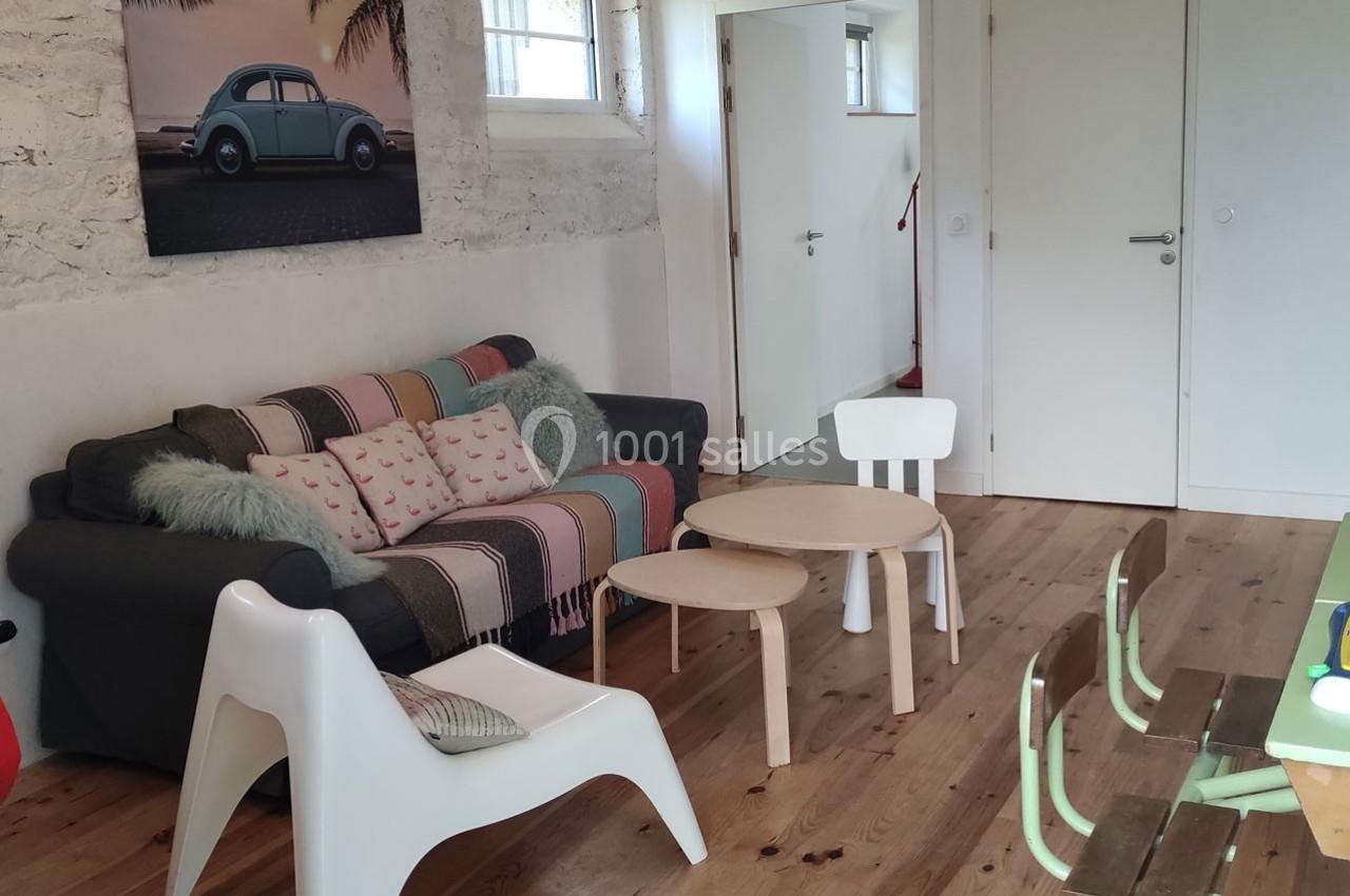 Salon avec canapé gris, tables basses en bois clair, chaises et décoration murale représentant une voiture vintage.