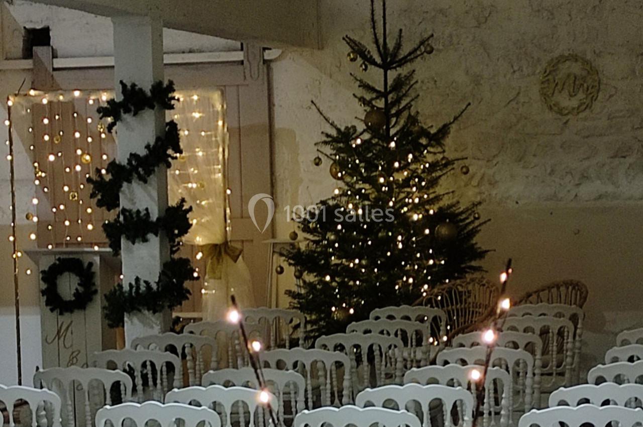 Salle décorée pour une fête avec des chaises blanches, un sapin illuminé et des guirlandes lumineuses.
