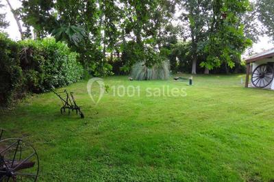 Un jardin verdoyant avec pelouse, arbres, arbustes et une charrette ancienne près d'un abri en bois.