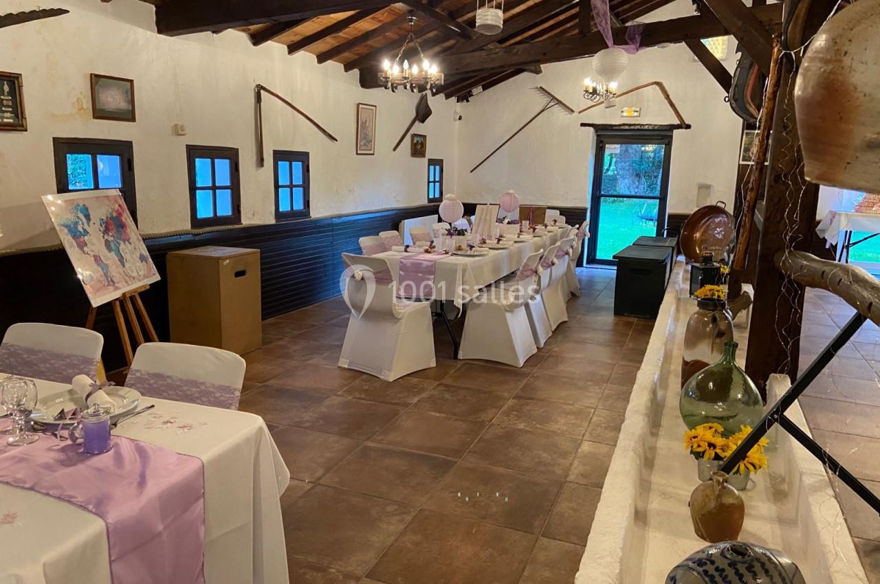 Salle décorée pour un événement avec des tables dressées, nappes violettes et éléments rustiques sur les murs.