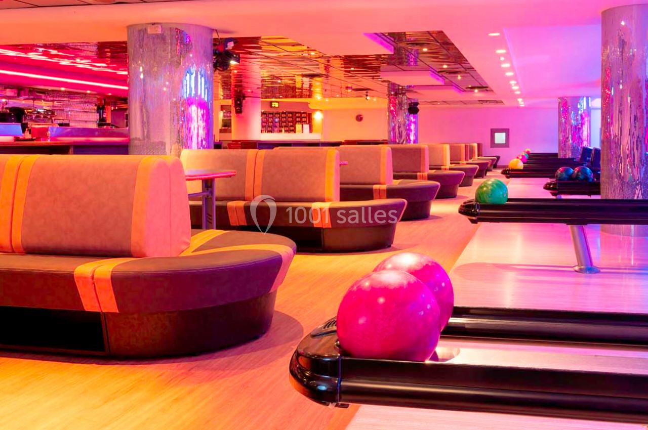 Salle de bowling moderne avec pistes alignées, boules colorées et banquettes éclairées par des lumières vives.