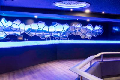 Entrée d'un espace moderne avec éclairage bleu, tapis rouge et panneau lumineux affichant un logo.