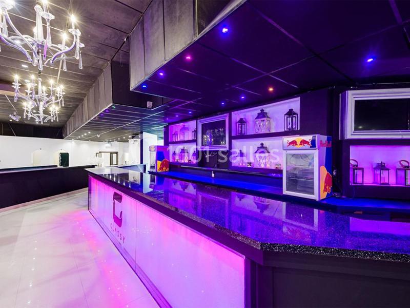 Comptoir de bar moderne avec éclairage violet, étagères décorées de lanternes et ambiance lumineuse.