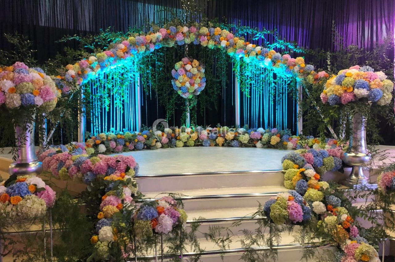 Décor floral coloré avec des arches et des arrangements de fleurs sur une scène surélevée, éclairée par des lumières…