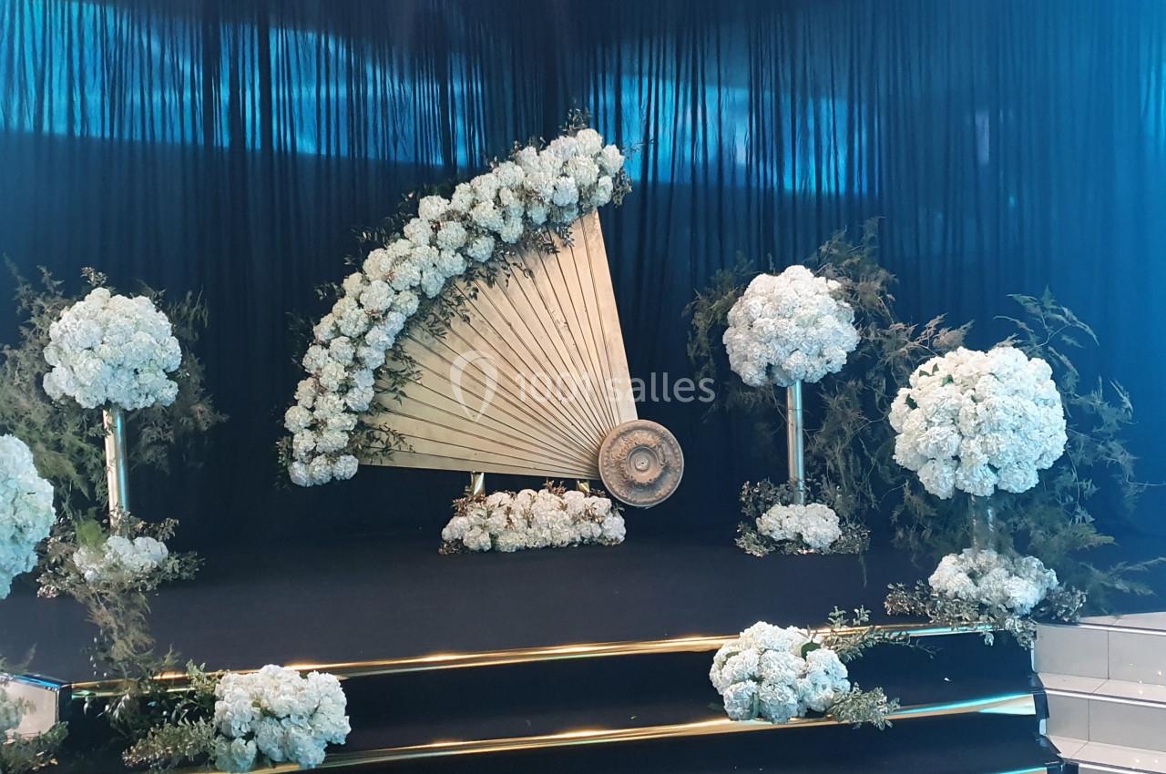 Décor floral élégant avec des bouquets blancs et un éventail géant en bois sur une scène sombre.