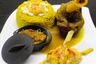 Assiette composée de riz safrané garni d'amandes et raisins secs, jarret d'agneau en sauce et accompagnements.