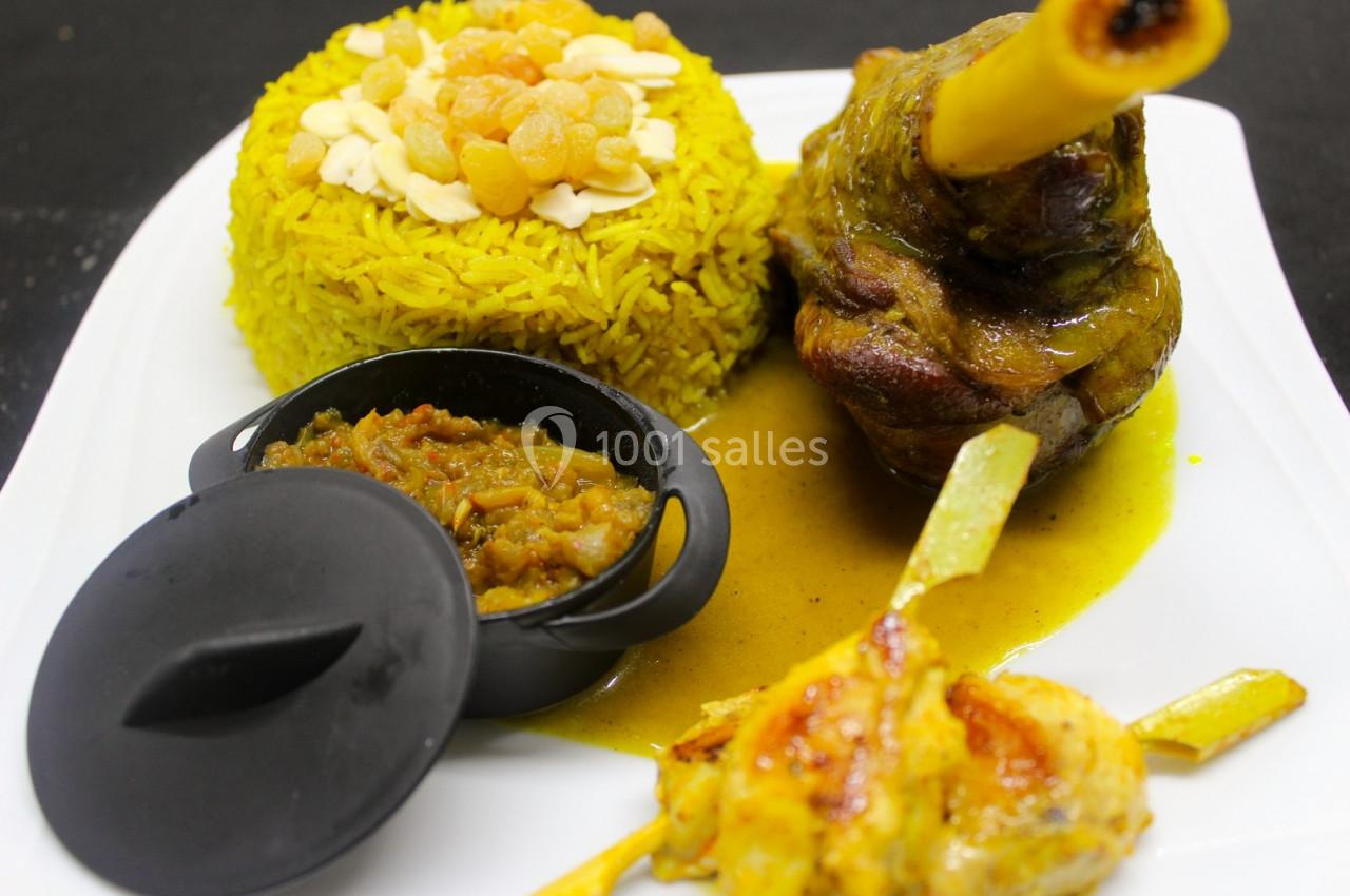 Assiette composée de riz safrané garni d'amandes et raisins secs, jarret d'agneau en sauce et accompagnements.