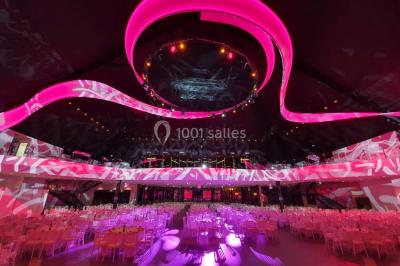 Tables rondes dressées avec nappes bleues alignées sur une pelouse, entourées d'arbres, avec un parc en arrière-plan.