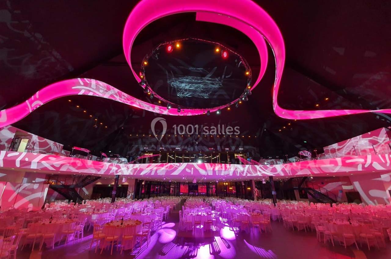Salle de réception spacieuse avec tables dressées et éclairages roses modernes au plafond.