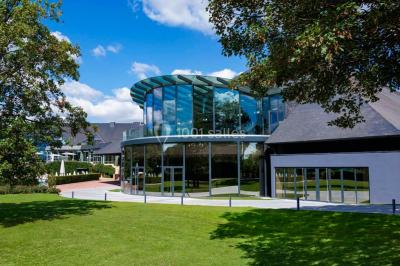 Tables rondes dressées avec nappes bleues alignées sur une pelouse, entourées d'arbres, avec un parc en arrière-plan.
