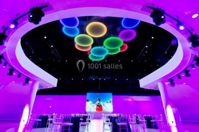 Tables rondes dressées avec nappes bleues alignées sur une pelouse, entourées d'arbres, avec un parc en arrière-plan.