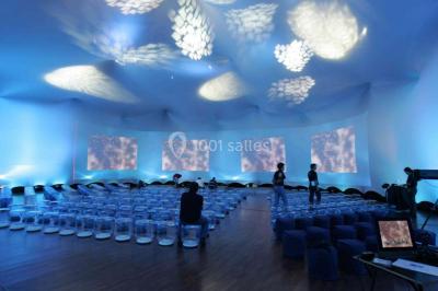 Tables rondes dressées avec nappes bleues alignées sur une pelouse, entourées d'arbres, avec un parc en arrière-plan.