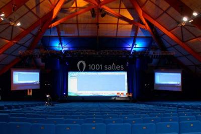 Tables rondes dressées avec nappes bleues alignées sur une pelouse, entourées d'arbres, avec un parc en arrière-plan.