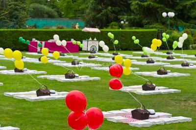 Tables rondes dressées avec nappes bleues alignées sur une pelouse, entourées d'arbres, avec un parc en arrière-plan.