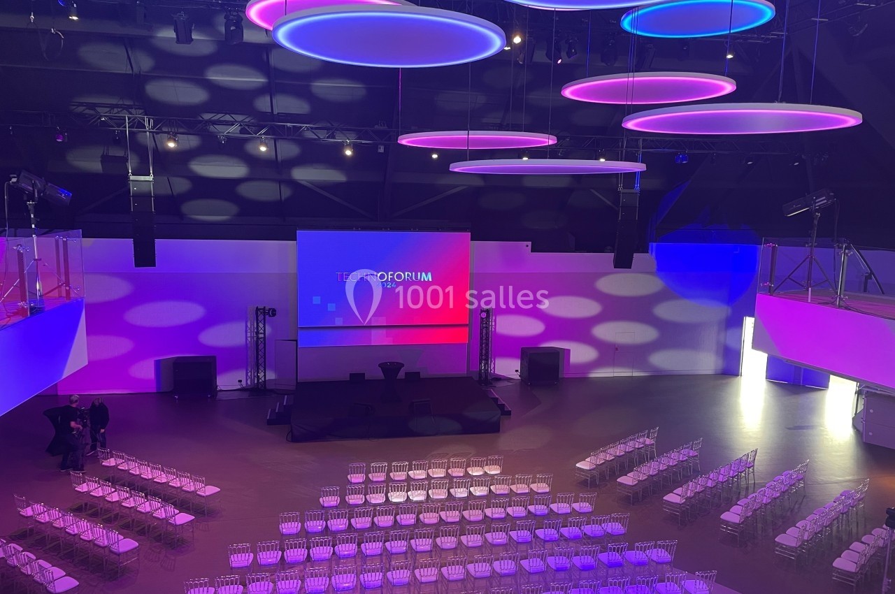 Salle de conférence moderne avec éclairage coloré, écran principal et rangées de chaises transparentes installées.