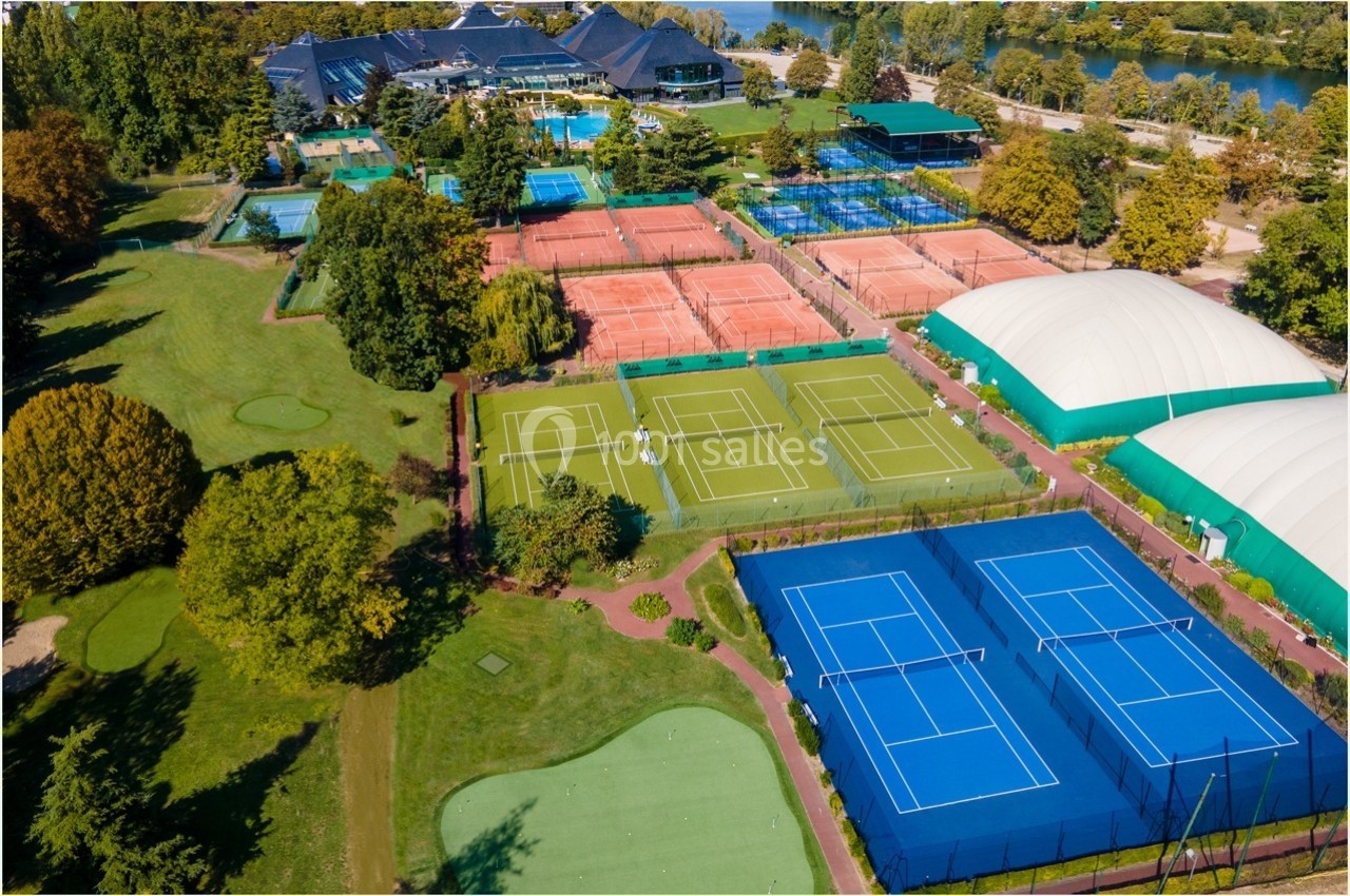 Vue aérienne d'un complexe sportif avec terrains de tennis en terre battue, gazon synthétique et courts couverts.