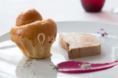 Dessert en forme de cœur au chocolat sur une assiette blanche, accompagné de coulis rouge et d'une verrine en arrière-plan.