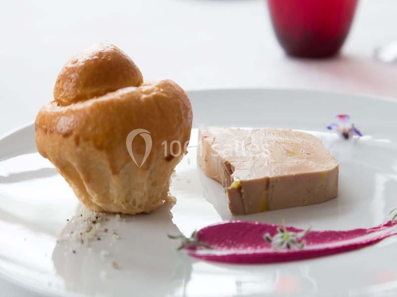 Assiette avec une tranche de foie gras, une brioche dorée et une décoration de purée rose et fleurs comestibles.