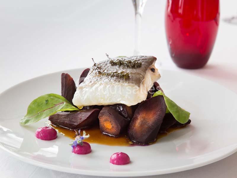 Filet de poisson sur un lit de carottes violettes, sauce et garniture végétale, présenté sur une assiette blanche.