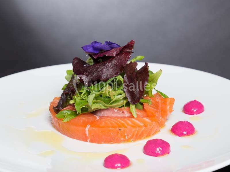 Assiette de saumon fumé garni de jeunes pousses, fleurs comestibles et points de sauce rose.