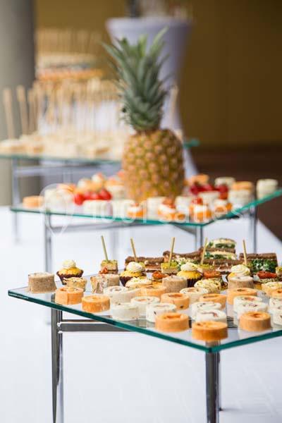Plateaux de bouchées apéritives variées disposés sur des supports en verre, avec un ananas en arrière-plan.