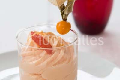 Mousse orange servie dans un verre, décorée d'un physalis et d'un segment de pamplemousse, posée sur une napperon blanc.