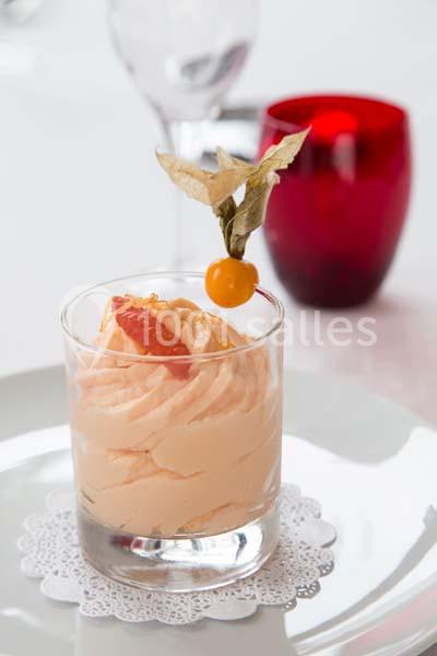 Mousse orange servie dans un verre, décorée d'un physalis et d'un segment de pamplemousse, posée sur une napperon blanc.