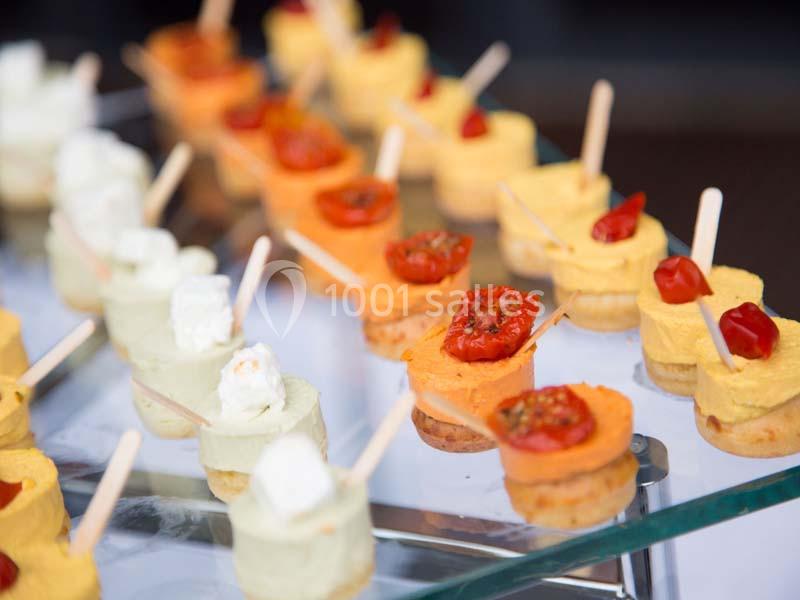 Assortiment de bouchées apéritives colorées avec mousse, tomates cerises et bâtonnets en présentation sur un plateau.