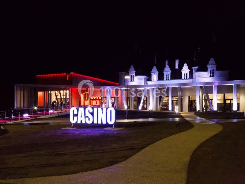 Façade d'un casino éclairé la nuit avec enseigne lumineuse et bâtiment principal aux tons rouges et blancs.
