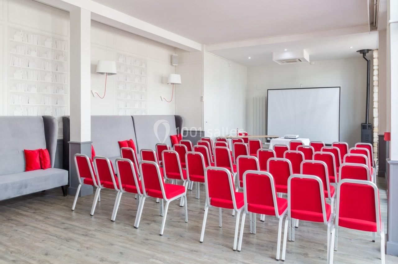 Salle de conférence lumineuse avec des chaises rouges alignées face à un écran de projection blanc.